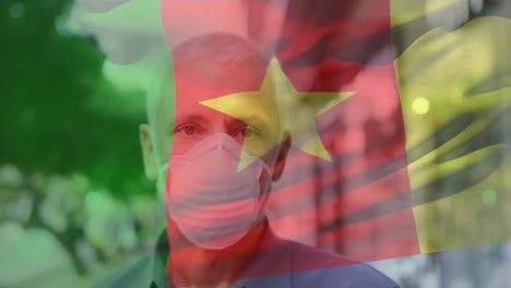 Animation-of-flag-of-cameroon-waving-over-caucasian-man-wearing-face-mask-in-city-street
