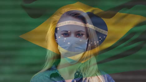 Animation-of-flag-of-brazil-waving-over-caucasian-woman-wearing-face-mask-in-city-street