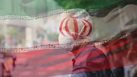 Animation-of-flag-of-iran-waving-over-caucasian-man-wearing-face-mask-in-city-street