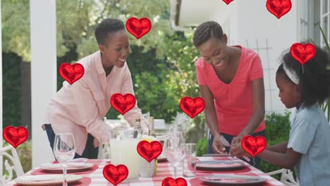Animation-of-heart-balloons-over-happy-african-american-family-preparing-dinner-in-garden