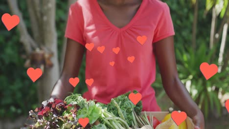Animation-of-hearts-over-happy-african-american-woman-holding-box-with-vegetables