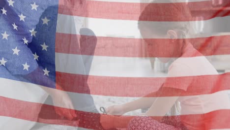 Animation-of-flag-of-usa-waving-over-caucasian-girl-tying-shoes-to-her-father