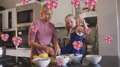 Animation-of-flower-hearts-over-caucasian-mother-and-daughter-cooking-together