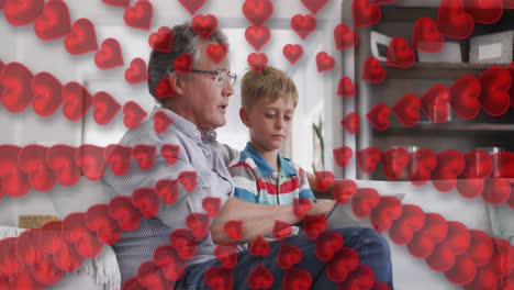Animation-Von-Herzen-über-Einem-Glücklichen-Kaukasischen-Großvater-Und-Enkel,-Die-Ein-Tablet-Auf-Dem-Sofa-Benutzen