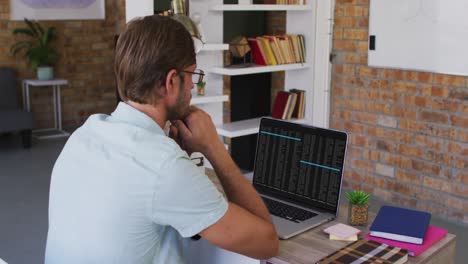 Caucasian-man-sitting-at-desk-watching-coding-data-processing-on-laptop-screen