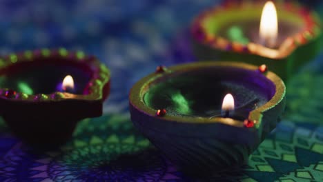 Lit-candles-in-decorative-clay-pots-on-patterned-table-top,-focus-on-foreground,-bokeh-background
