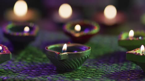 Lit-candles-in-decorative-clay-pots-on-woven-table-mat,-focus-on-foreground,-bokeh-background