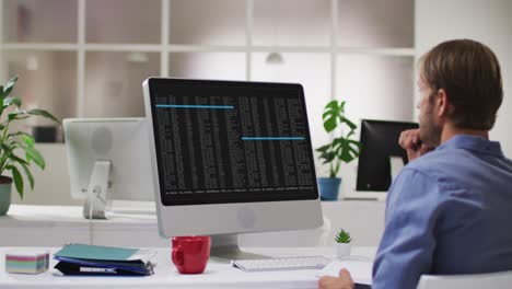 Caucasian-man-sitting-at-desk-watching-coding-data-processing-on-computer-screen