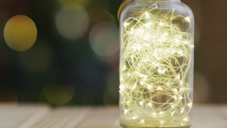 Video-of-wooden-table-with-fairy-lights-in-jar-over-christmas-tree