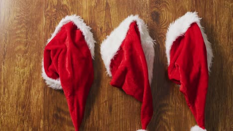 Video-of-three-santa-hats-hanging-in-a-row-on-wooden-background