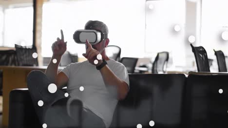 Animation-of-spots-over-caucasian-businessman-using-vr-headset-in-office