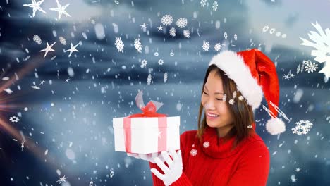 Animation-of-snow-falling-over-happy-asian-woman-wearing-santa-hat-keeping-present