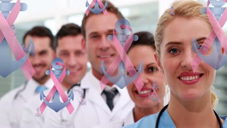 Animation-of-pink-ribbon-and-anchor-logos,-floating-over-smiling-group-of-male-and-female-doctors