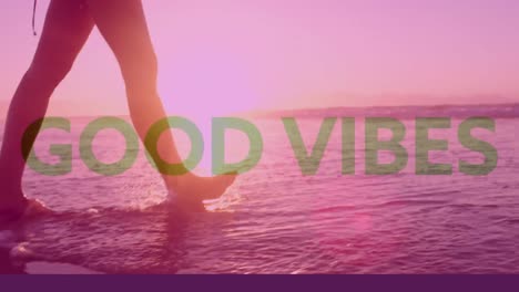 Animation-of-good-vibes-text-over-woman-walking-on-beach-into-sea-with-pink-tint