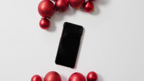 Video-of-red-christmas-baubles-and-smartphone-on-white-background