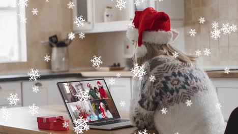 Animation-Von-Schnee,-Der-über-Eine-Glückliche-Kaukasische-Frau-Mit-Weihnachtsmütze-Bei-Einem-Laptop-Videoanruf-Fällt