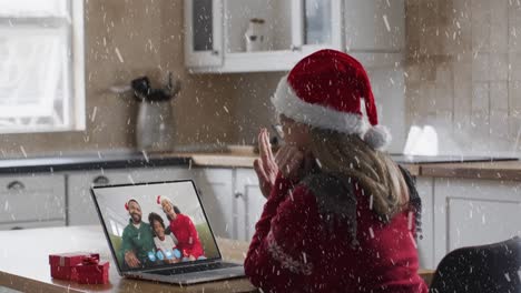 Animation-of-snow-falling-over-happy-caucasian-woman-in-santa-hat-on-laptop-video-call