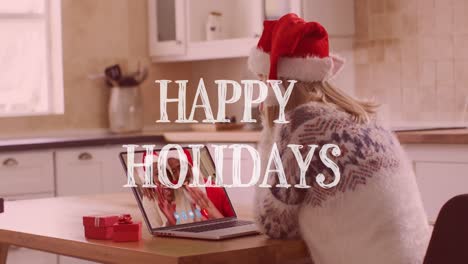 Animation-of-happy-holidays-text-over-happy-caucasian-woman-in-santa-hat-on-laptop-video-call