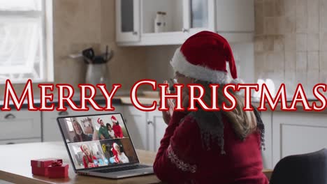 Animation-of-merry-christmas-text-over-happy-caucasian-woman-in-santa-hat-on-laptop-video-call
