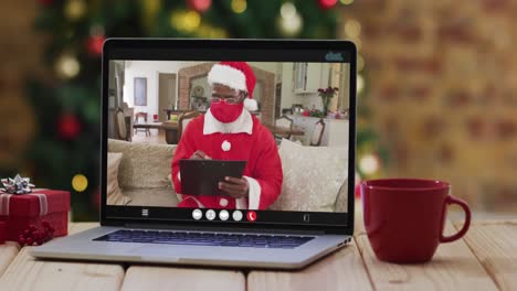 African-american-santa-in-face-mask-on-video-call-on-laptop,-with-christmas-tree