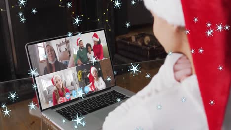 Animation-of-snow-falling-over-smiling-woman-in-santa-hat-on-laptop-video-call-with-her-family