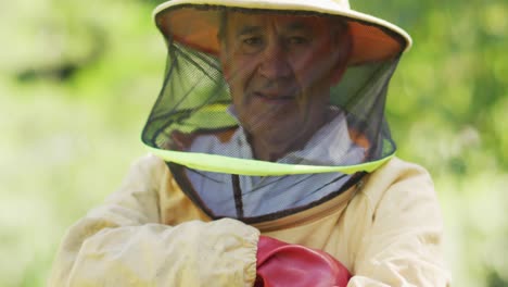 Portrait-of-smiling-caucasian-male-beekeeper-in-protective-clothing-with-arms-crossed