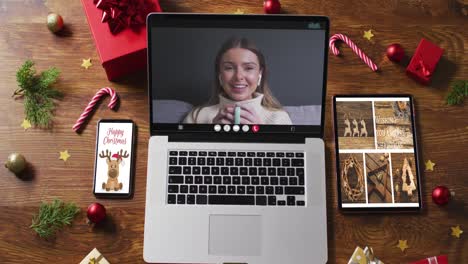 Happy-caucasian-woman-on-video-call-on-laptop,-with-smartphone,-tablet-and-christmas-decorations