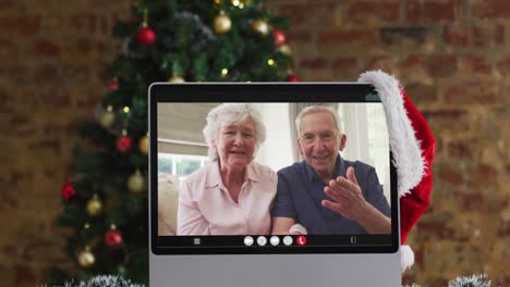 Caucasian-senior-couple-waving-on-video-call-on-computer,-with-christmas-tree