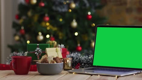 Laptop-with-green-screen-on-screen,-with-christmas-decorations-and-tree