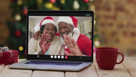 Pareja-De-Ancianos-Afroamericanos-Con-Sombreros-De-Santa-En-Videollamada-En-Una-Computadora-Portátil,-Con-árbol-De-Navidad