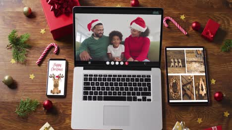 Family-wearing-snatas-hats-on-video-call-on-laptop,-with-smartphone,-tablet-and-decorations