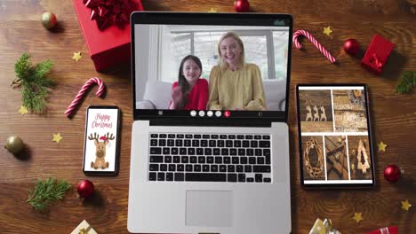 Mother-and-daughter-on-video-call-on-laptop,-with-smartphone,-tablet-and-christmas-decorations