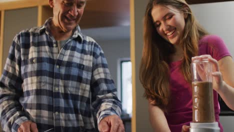 Smiling-senior-caucasian-father-and-teenage-daughter-preparing-health-drink-in-kitchen