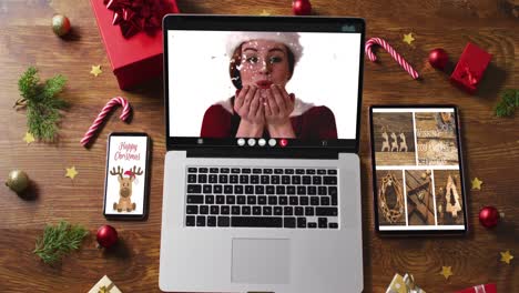 Caucasian-woman-in-santa-costume-on-video-call-on-laptop,-with-smartphone,-tablet-and-decorations