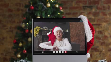 Happy-caucasian-woman-on-video-call-on-computer-,-with-christmas-decorations-and-tree