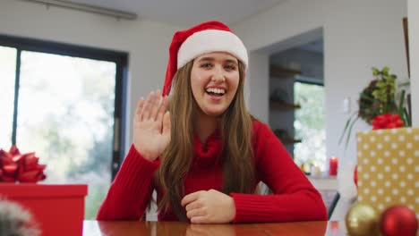 Mujer-Caucásica-Sonriente-Con-Sombrero-De-Papá-Noel-Haciendo-Videollamadas-En-Casa-Saludando