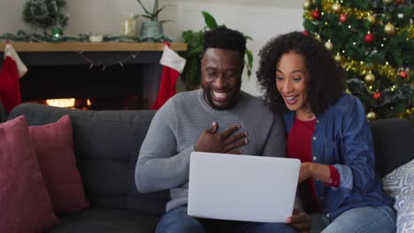 Smiling-african-american-couple-having-video-call-and-gesturing,-christmas-decorations-in-background
