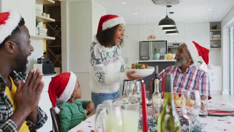 Happy-african-american-multi-generation-family-wearing-santa-hats-and-celebrating-in-kitchen