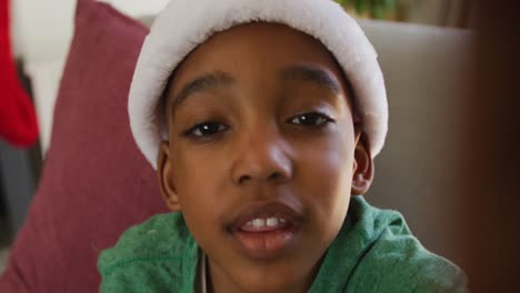 Happy-african-american-boy-wearing-santa-hat-having-video-call-at-christmas-time