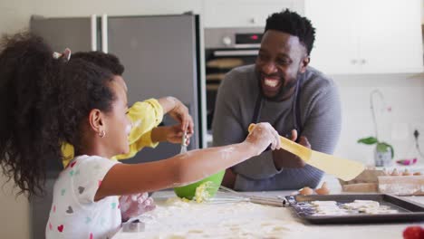 Happy-african-american-father-and-daughter-making-cookies-together-in-kitchen