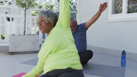 Glückliches-Afroamerikanisches-Seniorenpaar,-Das-Yoga-Auf-Einer-Matte-Auf-Der-Terrasse-Praktiziert