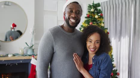 Glückliches-Afroamerikanisches-Paar,-Das-Sich-Umarmt-Und-In-Die-Kamera-Blickt,-Weihnachtsdekorationen-Im-Hintergrund