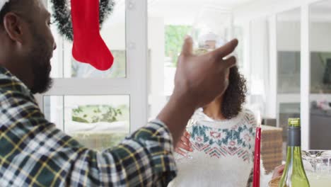 Glückliches-Afroamerikanisches-Paar,-Das-Weihnachtsmützen-Trägt-Und-In-Der-Küche-Feiert