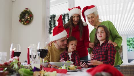 Glückliche-Kaukasische-Mehrgenerationenfamilie-Mit-Weihnachtsmützen-Und-Blick-Auf-Das-Smartphone