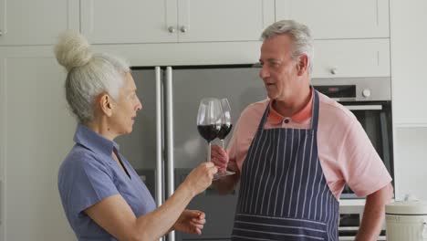 Glückliches-Kaukasisches-Seniorenpaar-Mit-Schürzen,-Das-Kocht-Und-Wein-Trinkt