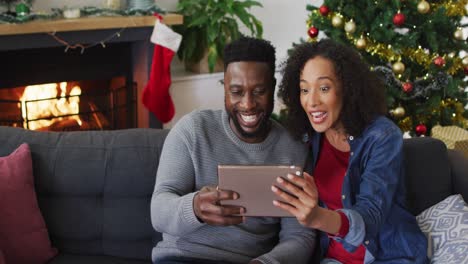 Lächelndes-Afroamerikanisches-Paar,-Das-Einen-Videoanruf-Führt-Und-Gestikuliert,-Weihnachtsdekorationen-Im-Hintergrund