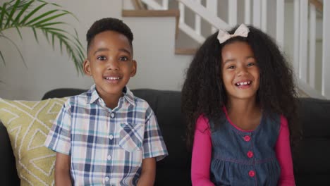 African-american-siblings-siting-on-sofa,-looking-at-camera-and-smiling