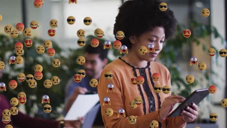 Animation-Digitaler-Emoji-Symbole-über-Einer-Lächelnden-Geschäftsfrau-Mit-Gemischter-Rasse,-Die-Ein-Tablet-Verwendet