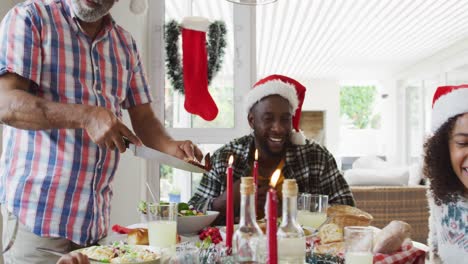 Happy-african-american-multi-generation-family-wearing-santa-hats-and-celebrating-holiday-meal