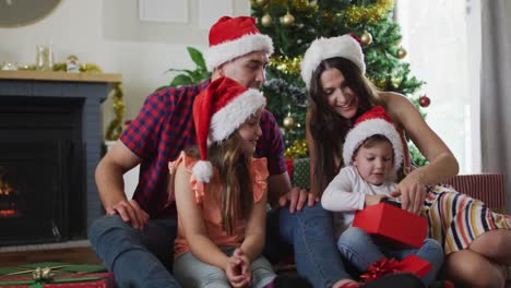 Glückliche-Kaukasische-Familie,-Die-Weihnachtsmützen-Trägt-Und-Geschenke-Auspackt